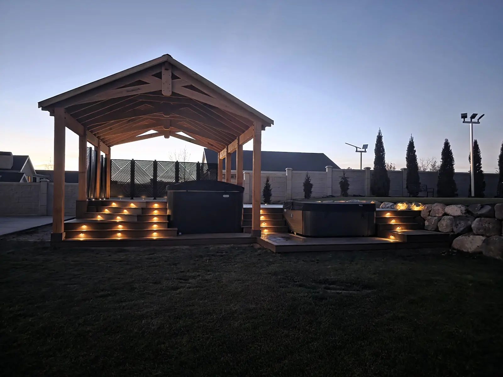 Timber pavilion and two hot tub decks with lit stairs at dusk