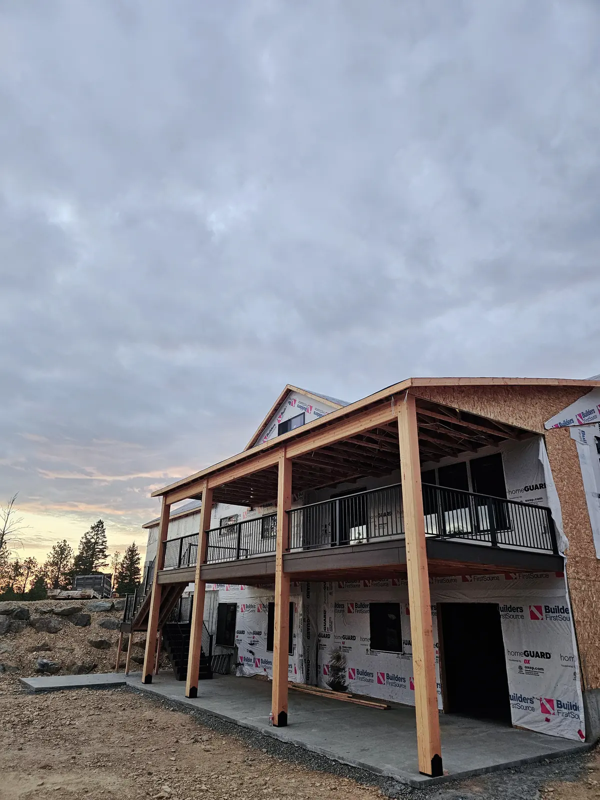 Covered second-story deck with timber posts and black railing on a new home at sunset