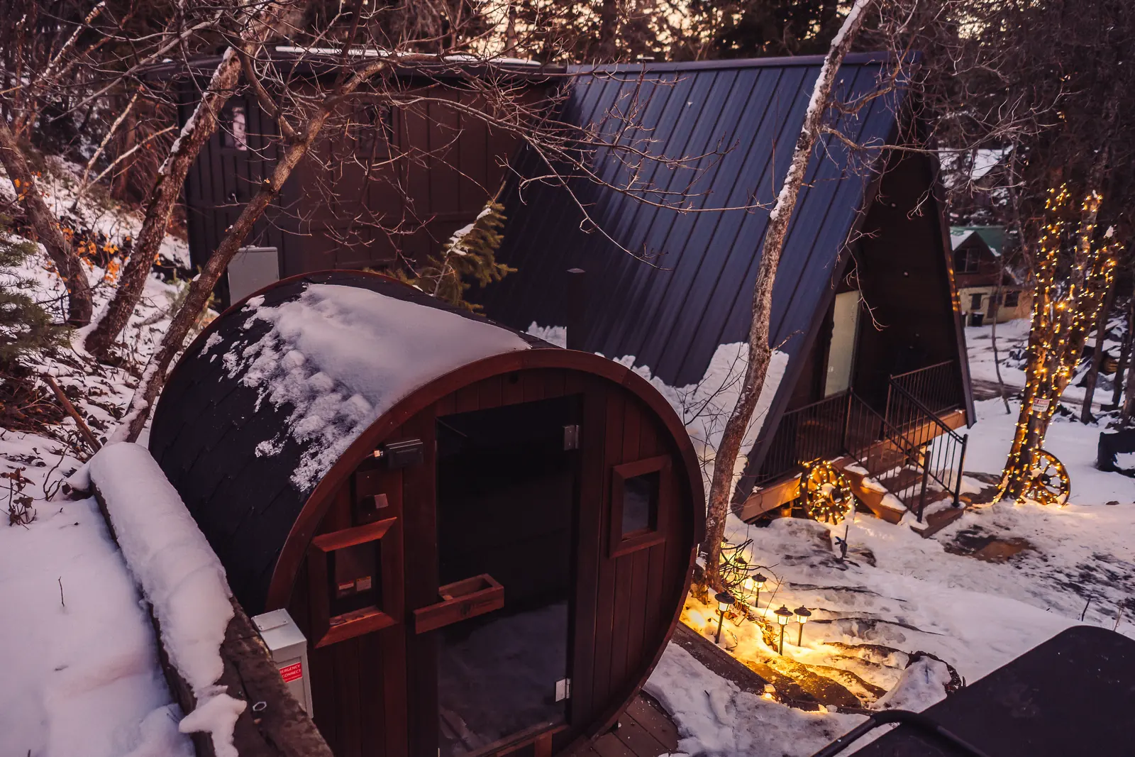 Barrel sauna on a new deck beside an A-frame cabin in winter